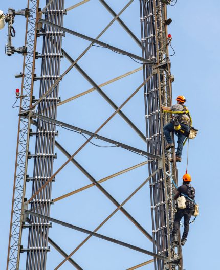 Communication maintenance. Two technicians climbing on telecom tower antenna against blue sky background